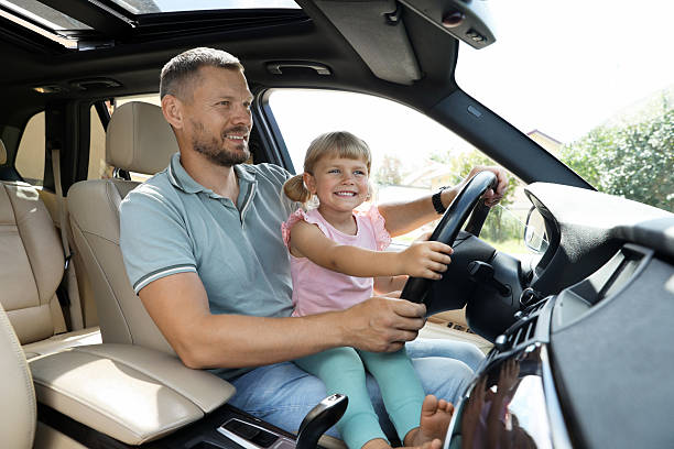 istock Happy man with his daughter holding steering wheel inside car 2209685485