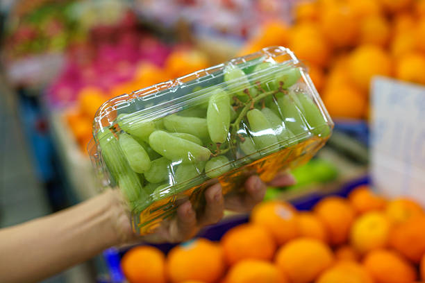 istock Hand holding a plastic container of green grapes in a fruit market 2209686599