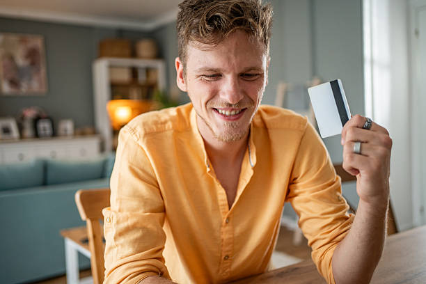 istock Young man smiling and holding credit card at home 2209689828