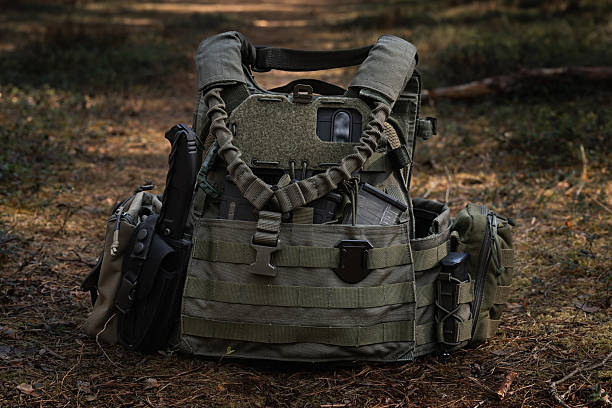 Olive tactical vest with smartphone for navigation, tactical knife, and pouches in the forest.