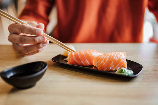 Unrecognizable man eating nigiri sushi with salmon.