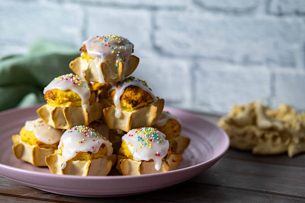 A plate of small Easter sweets, typical of Sardinia. The name of the sweet is Pardulas, made with ricotta, oranges, saffron and eggs. The sweets are covered with sugar icing and colored sprinkles and look delicious. In the background the artistic bread also typical of the holidays.
