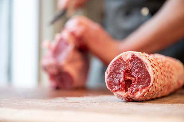 Selective focus of butcher slicing raw lamb and rolling it in gourmet butcher shop, Vancouver, B.C.
