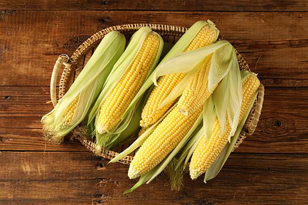 istock Many fresh ripe corncobs with green husks on wooden table, top view 2209696965