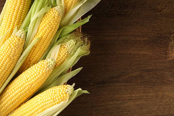 istock Many fresh ripe corncobs with green husks on wooden table, top view. Space for text 2209697055