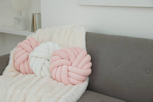 istock Different soft pillows in shape of knot and blanket on sofa in room 2209698699