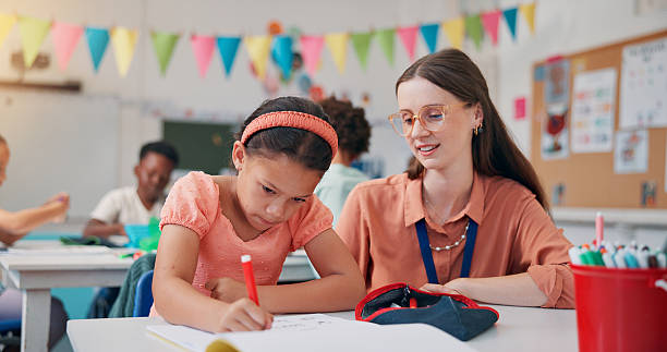 istock Writing, girl and teacher in classroom, learning and advice with literacy knowledge. Child development, woman or students in school, education or test with assessment, questions and fine motor skills 2209704821