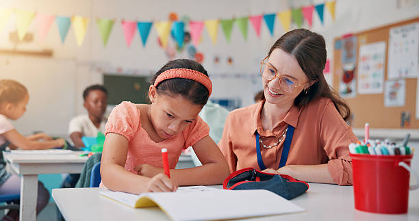 istock Education, girl and teacher with help, writing and child development with literacy knowledge. Support, woman or students in school, assisted learning or advice with assessment and growth in classroom 2209704848