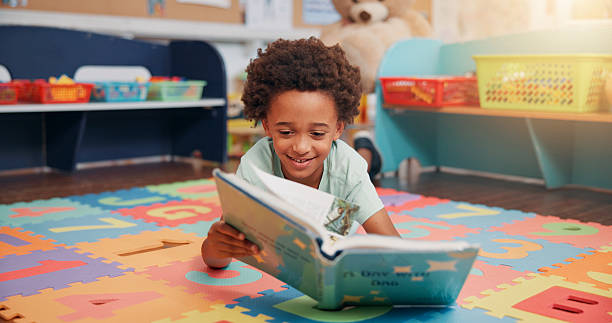 istock Boy, reading book and education on floor in classroom for development, storytelling or knowledge at academy. Child, learning and study for scholarship, smile or info with course at elementary school 2209704878