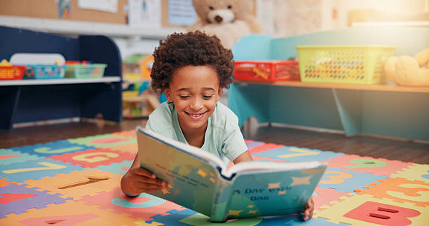 istock African boy, reading book and floor in classroom for development, storytelling and knowledge at academy. Child, learning and study for scholarship, smile or info with course at elementary school 2209704901