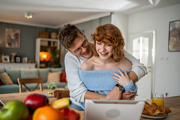 istock Happy couple embracing and laughing while video calling on tablet at home 2209708403