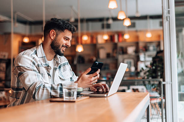 istock Young man working remotely using laptop and smartphone in a cafe 2209711790