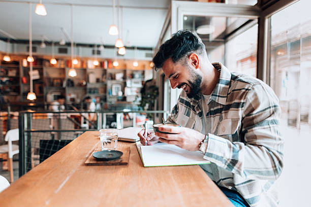 istock Young man writing notes and drinking coffee in a bookstore cafe 2209712093
