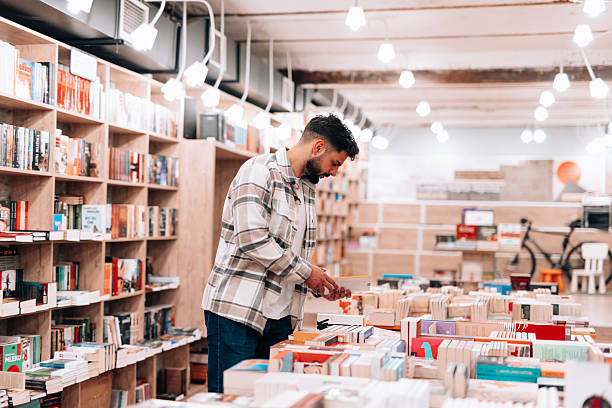 Young bearded man browsing through shelves in a cozy bookstore, searching for an intriguing book to dive into, surrounded by a diverse collection of literature and knowledge
