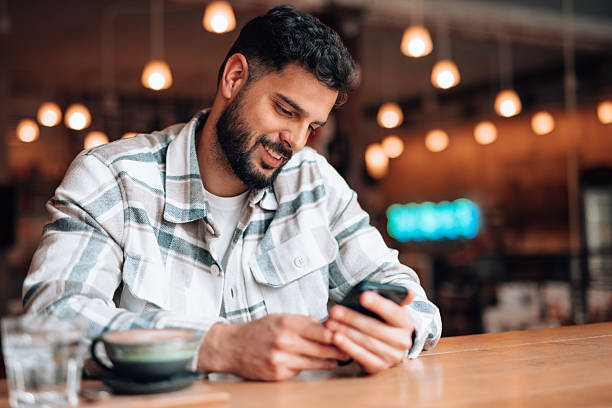 istock Young man smiling and using mobile phone in a cafe 2209713522