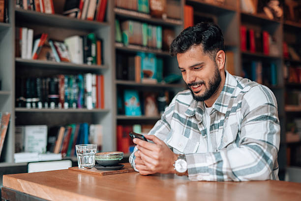istock Young man using phone in a coffeeshop with library background 2209713587
