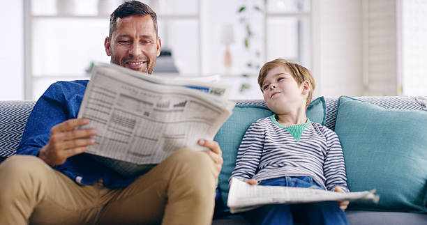 istock Home, father and child with newspaper for reading, article updates and cognitive development on sofa. Happy people, dad and boy with information for knowledge, current events and bonding in lounge 2209721486