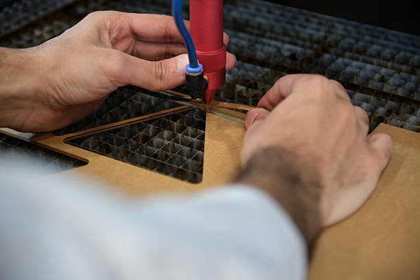 A detailed view of hands using a laser cutting machine for precise fabrication. The image depicts technical precision, craftsmanship, and the use of modern manufacturing technology in industrial or creative settings.