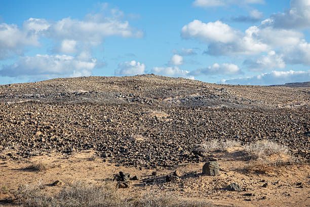 Desolate Beauty Near La Santa – A cracked lava field stretches toward Lanzarote’s coast, where stubborn drought-resistant plants cling to life between volcanic boulders. The surreal, Mars-like terrain contrasts with the distant blue Atlantic, embodying the island’s raw, minimalist allure.