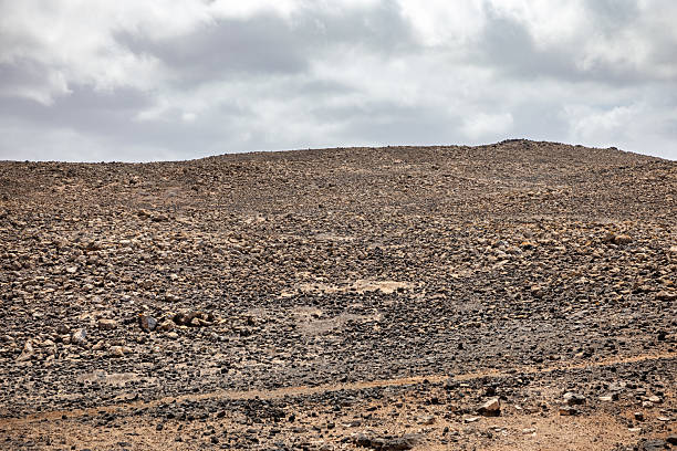 Desolate Beauty Near La Santa – A cracked lava field stretches toward Lanzarote’s coast, where stubborn drought-resistant plants cling to life between volcanic boulders. The surreal, Mars-like terrain contrasts with the distant blue Atlantic, embodying the island’s raw, minimalist allure.
