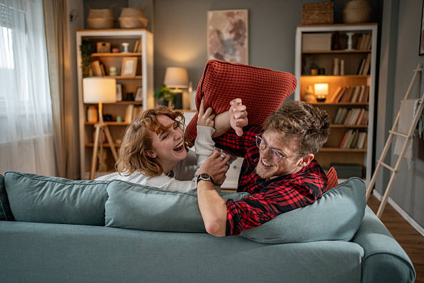 istock Young couple pillow fighting on sofa in living room having fun 2209724113