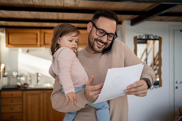 istock Father multitasking: holding daughter, reading document, and talking on phone 2209724750