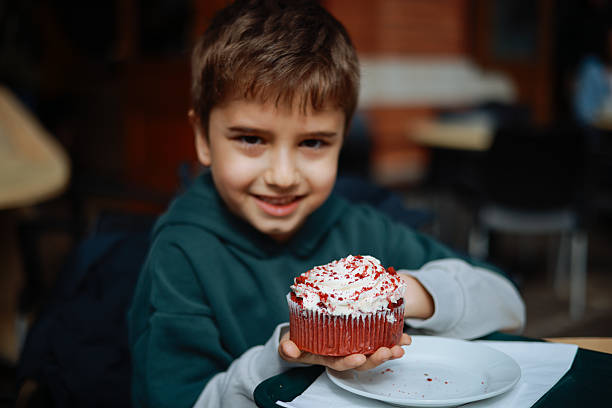 A young boy wearing an orange jacket and a blue knit hat is holding a slice of pizza while sitting at an outdoor table. The boy appears happy and engaged, creating a warm and inviting scene perfect for advertising family dining or casual food events