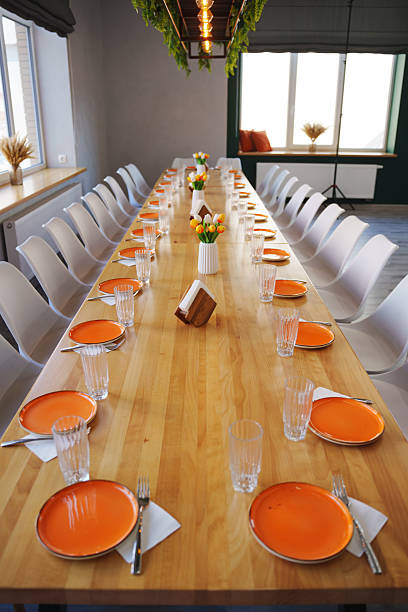 istock Long dining table set for a gathering with orange plates and floral centerpieces 2209730418