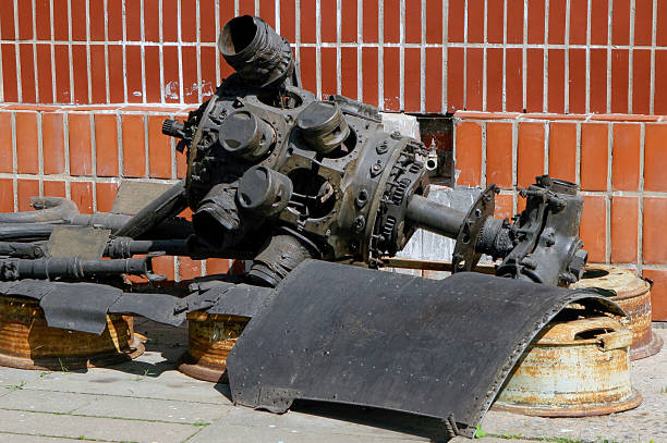 Rusty mechanical components are scattered on the ground next to a bright red brick wall in a city.