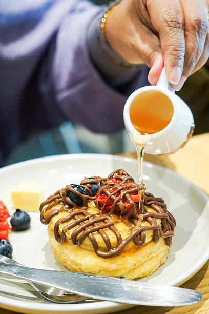Close-up of a person pouring syrup onto pancakes
