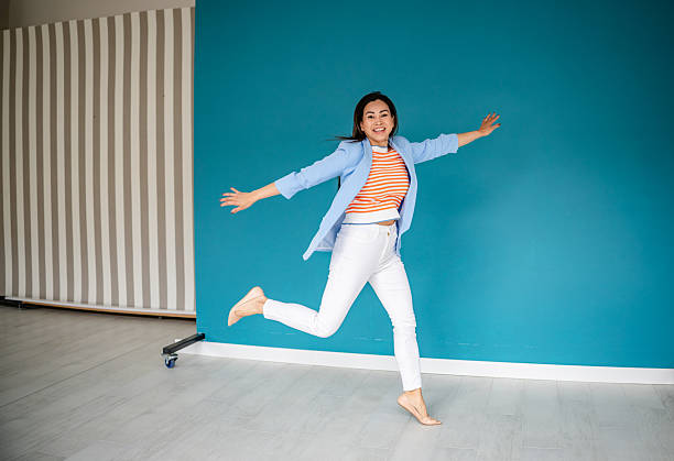 A joyful young woman expresses her happiness through dance in a stylish, indoor space. She wears casual attire and radiates confidence while having fun.