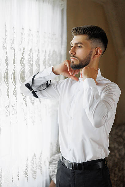 istock A man in a white shirt and black pants is getting ready to tie his tie 2209739759