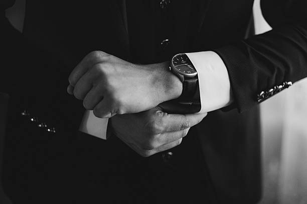 A man is wearing a black suit and is looking at his watch