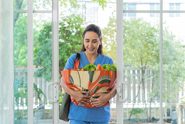 istock Smiling Nurse Returning Home with Fresh Groceries in a Reusable Bag 2209748534