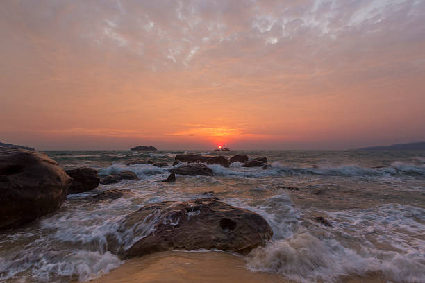 Rocky beach at sunset with waves and orange sky in Cambodia