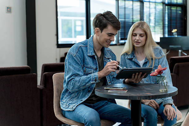 istock Young couple in denim jackets using digital tablet together at a table in a stylish lounge area, discussing travel plans or working in a relaxed environment 2209752227