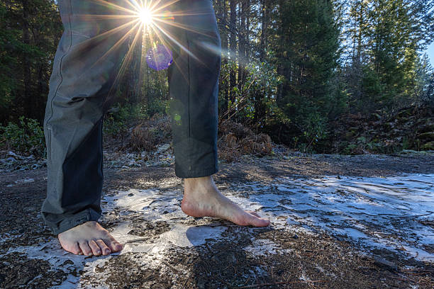 Human feet of an adult male walking barefoot on a frozen puddle as a form of grounding and connection to the earth.