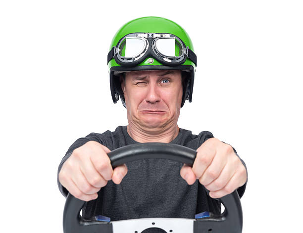istock Funny man in a green helmet and goggles making a scared face while gripping a steering wheel tightly. Isolated on white background. File contains a path to isolation. Concept of fear. 2209763109