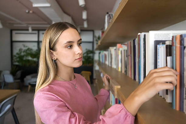 istock Serious beautiful student girl taking textbook for studying from bookshelf 2209764063