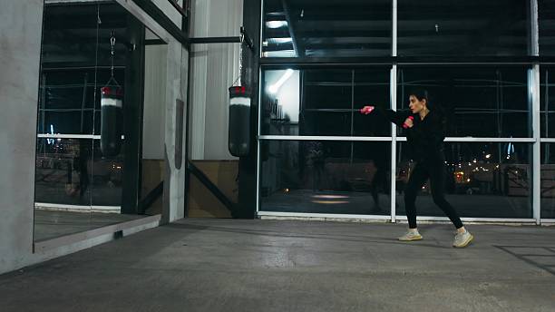 istock Young woman practicing boxing punches in empty gym at night 2209766643