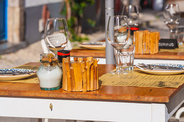 A cozy wooden table with a colorful striped table runner is elegantly decorated with a vibrant red flower in a clear glass vase and a small decorative metallic object. The setting suggests a warm, intimate restaurant ambiance, with wooden chairs around the table and softly lit surroundings in the background.