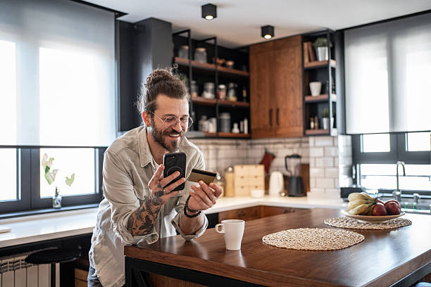 istock Young man making online payment using credit card and smartphone in kitchen 2209774633
