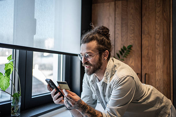 istock Young man making online payment using smartphone and credit card at home 2209775217