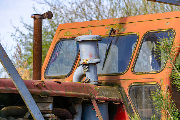 An old, rusty tractor cab covered in moss and lichen, partially obscured by branches.