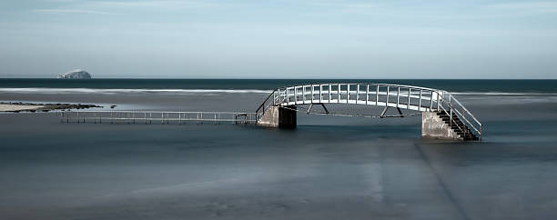 Belhaven Bridge crosses the River Biel by the beach at Dunbar, Scotland.  At high tide, the base of the bridge and the path leading to it is submerged, giving the iconic vista shown in this image.  The Bass Rock may also be seen in the background.