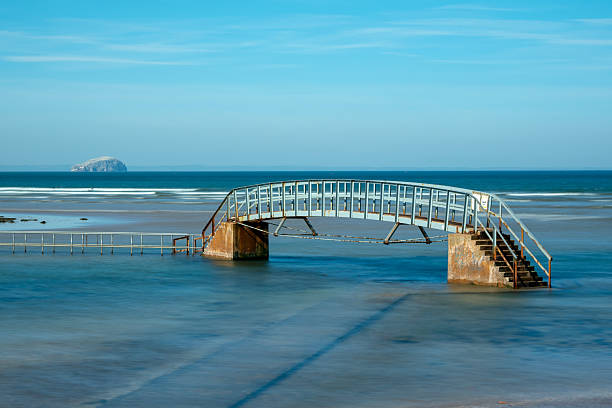 Belhaven Bridge crosses the River Biel by the beach at Dunbar, Scotland.  At high tide, the base of the bridge and the path leading to it is submerged, giving the iconic vista shown in this image.  The Bass Rock may also be seen in the background.