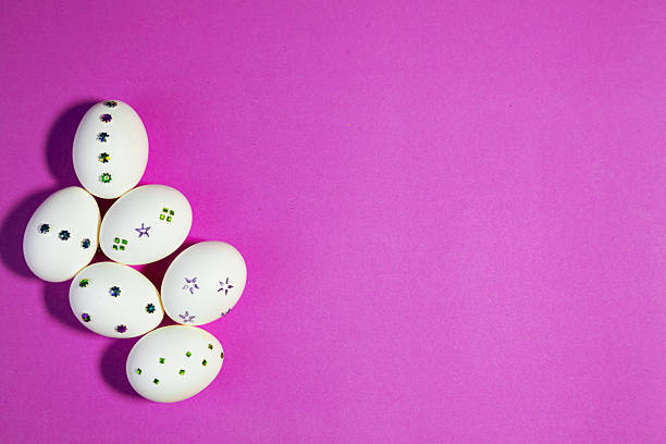 Top View of Sparkling White Easter Eggs on Purple. Flat lay composition showing sparkling Easter eggs on orange background, representing joy, festivity, and spring celebration.
