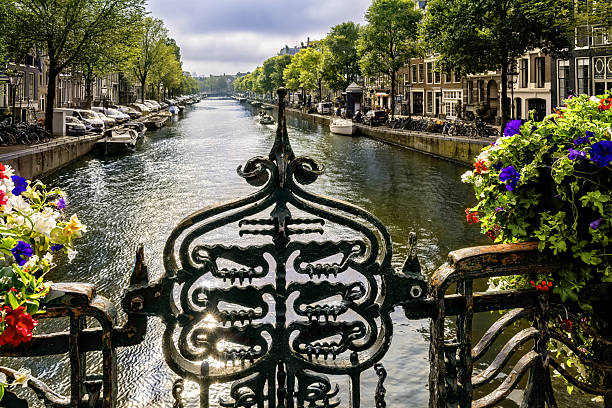 Woman riding bicycle on historic bridge in Amsterdam. Scenic view of traditional buildings and calm canal. Urban cityscape with active lifestyle and European architecture.