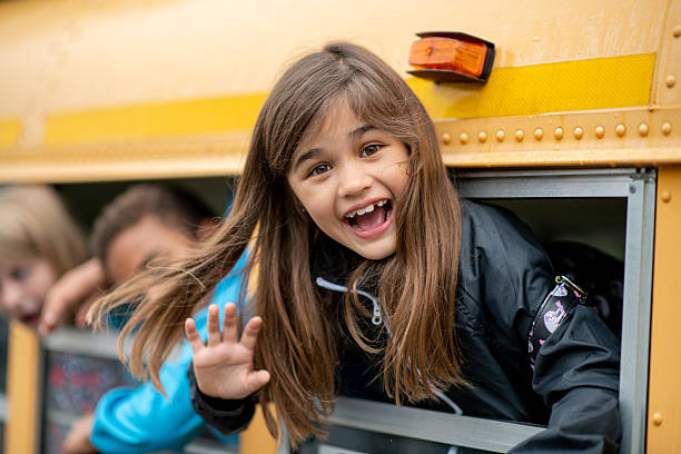 A cute elementary age girl smiles and walks down the aisle of a school bus to get off at her bus stop.