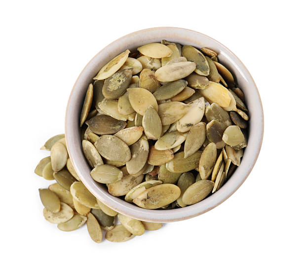 istock Peeled pumpkin seeds in bowl isolated on white, top view 2209792368